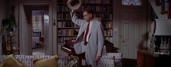 Movie still from “The Seven Year Itch” (1955), directed by Billy Wilder – A man in a suit throwing a frisbee in a room; Medium shot, High angle
