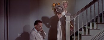 Movie still from “The Seven Year Itch” (1955), directed by Billy Wilder – A man sitting in front of a woman in a dress; Wide shot, Low angle
