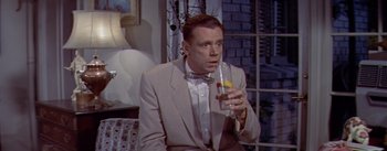 Movie still from “The Seven Year Itch” (1955), directed by Billy Wilder – A man wearing a suit and tie holding a glass of water; Medium shot, High angle