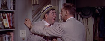 Movie still from “The Seven Year Itch” (1955), directed by Billy Wilder – Two men in suits and a hat are laughing together; Medium shot, Over the shoulder angle