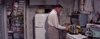 Movie still from “The Seven Year Itch” (1955), directed by Billy Wilder – A man standing at a sink in a kitchen preparing a meal; Medium shot, Low angle