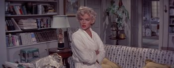 Movie still from “The Seven Year Itch” (1955), directed by Billy Wilder – A woman sitting on top of a couch in a living room; Medium shot, Over the shoulder angle