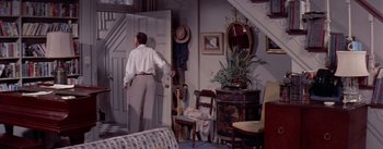 Movie still from “The Seven Year Itch” (1955), directed by Billy Wilder – A man standing in front of an open door in a living room; Wide shot, High angle