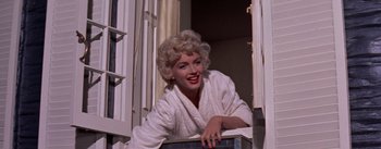 Movie still from “The Seven Year Itch” (1955), directed by Billy Wilder – A woman in a white bathrobe leaning against a window sill; Medium shot, Low angle