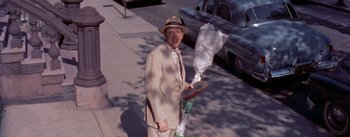 Movie still from “The Seven Year Itch” (1955), directed by Billy Wilder – An older man in a suit and hat holding an umbrella; Wide shot, High angle