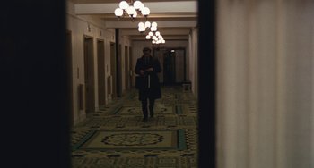 Movie still from “The Seven-Ups” (1973), directed by Philip D'Antoni – A person walking in a hallway with lights above them; Wide shot, Over the shoulder angle