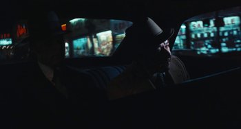 Movie still from “The Seven-Ups” (1973), directed by Philip D'Antoni – A man wearing a hat sitting in the back of a car; Medium shot, Over the shoulder angle