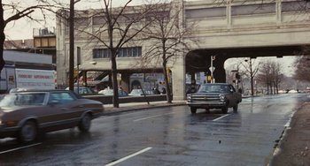 Movie still from “The Seven-Ups” (1973), directed by Philip D'Antoni – A car is driving down the street on a rainy day; Extreme Wide shot, High angle