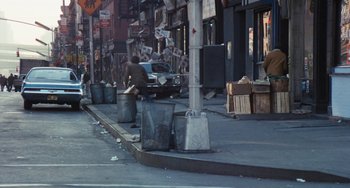 Movie still from “The Seven-Ups” (1973), directed by Philip D'Antoni – A man sitting on the side of the street next to trash cans; Wide shot, High angle