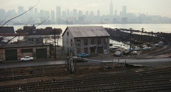 Movie still from “The Seven-Ups” (1973), directed by Philip D'Antoni – An old building sitting next to a train track next to a body of water; Extreme Wide shot, High angle