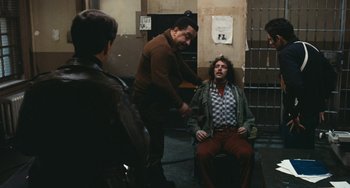 Movie still from “The Seven-Ups” (1973), directed by Philip D'Antoni – A man sitting on a chair in a room; Wide shot, Over the shoulder angle