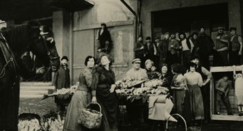 Movie still from “The Ship Sails On” (1983), directed by Federico Fellini – A group of people standing next to each other at an outdoor market; Wide shot, High angle