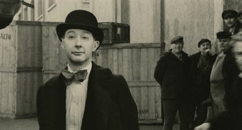 Movie still from “The Ship Sails On” (1983), directed by Federico Fellini – A man wearing a hat and a bow tie standing next to another man; Close Up shot, Over the shoulder angle