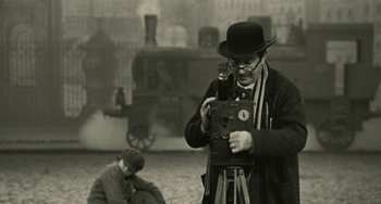 Movie still from “The Ship Sails On” (1983), directed by Federico Fellini – An older man is taking a picture with a camera; Medium shot, Low angle