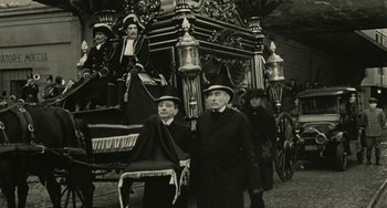 Movie still from “The Ship Sails On” (1983), directed by Federico Fellini – Two men and a woman standing in front of an elaborate carriage; Wide shot, High angle