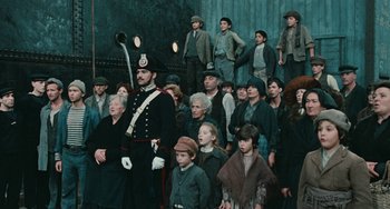 Movie still from “The Ship Sails On” (1983), directed by Federico Fellini – A group of people standing in a room with a soldier; Wide shot, High angle