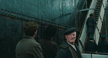 Movie still from “The Ship Sails On” (1983), directed by Federico Fellini – An older man wearing a hat standing in front of another man; Medium shot, Low angle