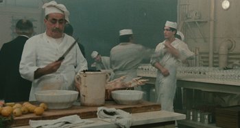 Movie still from “The Ship Sails On” (1983), directed by Federico Fellini – A group of chefs preparing food inside of a kitchen; Medium shot, High angle