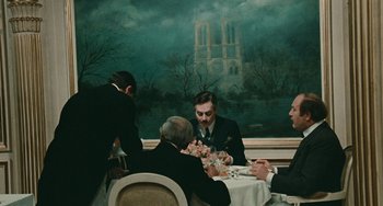 Movie still from “The Ship Sails On” (1983), directed by Federico Fellini – A group of people sitting at a table with food on it; Wide shot, Over the shoulder angle