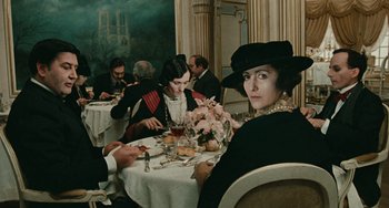 Movie still from “The Ship Sails On” (1983), directed by Federico Fellini – A group of people sitting at a table with plates of food; Medium shot, Over the shoulder angle