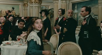 Movie still from “The Ship Sails On” (1983), directed by Federico Fellini – A young girl smiling in front of an older man and woman; Medium shot, Over the shoulder angle