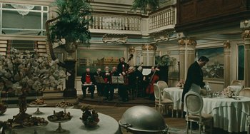 Movie still from “The Ship Sails On” (1983), directed by Federico Fellini – A group of people playing music inside of a room; Wide shot, High angle