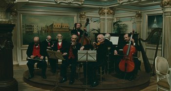 Movie still from “The Ship Sails On” (1983), directed by Federico Fellini – A group of men playing instruments in front of a painting; Wide shot, Low angle