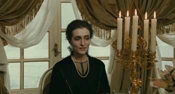 Movie still from “The Ship Sails On” (1983), directed by Federico Fellini – A woman sitting at a table in front of candles; Medium shot, Over the shoulder angle