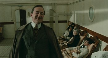 Movie still from “The Ship Sails On” (1983), directed by Federico Fellini – A group of people sitting in a room with a man in a suit; Medium shot, Low angle