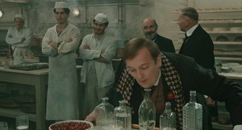 Movie still from “The Ship Sails On” (1983), directed by Federico Fellini – A group of men standing around a table with food on top of it; Medium shot, Over the shoulder angle