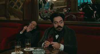 Movie still from “The Ship Sails On” (1983), directed by Federico Fellini – A man sitting at a table with a cigarette in his mouth; Medium shot, Over the shoulder angle