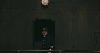 Movie still from “The Ship Sails On” (1983), directed by Federico Fellini – A man in a uniform standing next to a building; Wide shot, Low angle