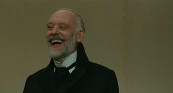 Movie still from “The Ship Sails On” (1983), directed by Federico Fellini – An older man wearing a black jacket and a black tie; Close Up shot, Low angle