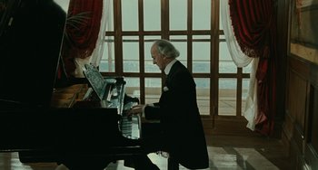 Movie still from “The Ship Sails On” (1983), directed by Federico Fellini – An older man in a black suit playing a piano; Medium shot, High angle