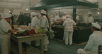 Movie still from “The Ship Sails On” (1983), directed by Federico Fellini – A group of people standing in a kitchen preparing food; Wide shot, High angle