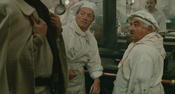 Movie still from “The Ship Sails On” (1983), directed by Federico Fellini – A group of people standing around in a kitchen; Medium shot, Over the shoulder angle
