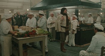 Movie still from “The Ship Sails On” (1983), directed by Federico Fellini – A group of people in a kitchen preparing food; Wide shot, Over the shoulder angle