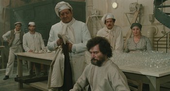 Movie still from “The Ship Sails On” (1983), directed by Federico Fellini – A group of men standing around a man with a long beard; Medium shot, Over the shoulder angle