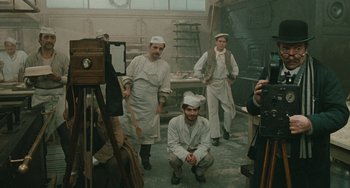 Movie still from “The Ship Sails On” (1983), directed by Federico Fellini – A group of men standing around in a room; Wide shot, High angle