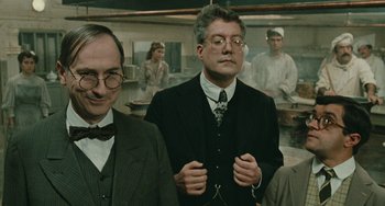 Movie still from “The Ship Sails On” (1983), directed by Federico Fellini – A group of men standing next to each other in a room; Medium shot, Low angle