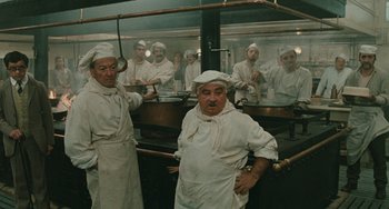Movie still from “The Ship Sails On” (1983), directed by Federico Fellini – A group of men standing in a kitchen preparing food; Medium shot, High angle