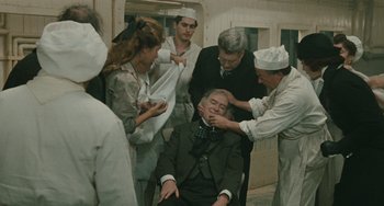 Movie still from “The Ship Sails On” (1983), directed by Federico Fellini – A group of people standing around an older man; Medium shot, High angle