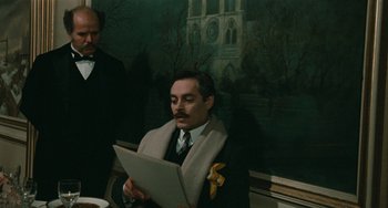 Movie still from “The Ship Sails On” (1983), directed by Federico Fellini – A man in a suit and tie holding a paper; Medium shot, Over the shoulder angle