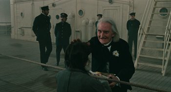Movie still from “The Ship Sails On” (1983), directed by Federico Fellini – An old man in a black suit is holding a rope; Medium shot, Over the shoulder angle