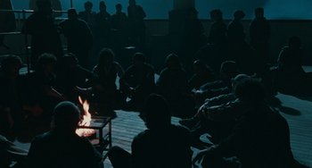 Movie still from “The Ship Sails On” (1983), directed by Federico Fellini – A group of people sitting around a fire at night; Wide shot, High angle