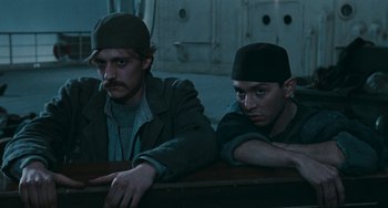 Movie still from “The Ship Sails On” (1983), directed by Federico Fellini – A couple of men sitting next to each other on top of a table; Medium shot, Low angle