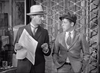 Movie still from “The Shop Around the Corner” (1940), directed by Ernst Lubitsch – Two men in suits and hats are standing next to each other holding papers; Medium shot, Over the shoulder angle