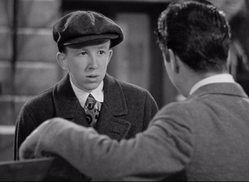 Movie still from “The Shop Around the Corner” (1940), directed by Ernst Lubitsch – A young man in a hat and a tie talking to a younger man; Close Up shot, Over the shoulder angle