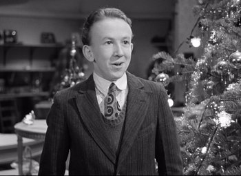 Movie still from “The Shop Around the Corner” (1940), directed by Ernst Lubitsch – A man in a suit and tie standing in front of a christmas tree; Medium shot, Low angle