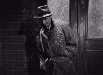 Movie still from “The Snake Pit” (1948), directed by Anatole Litvak – A man in a hat and a coat standing in front of a door; Medium shot, High angle